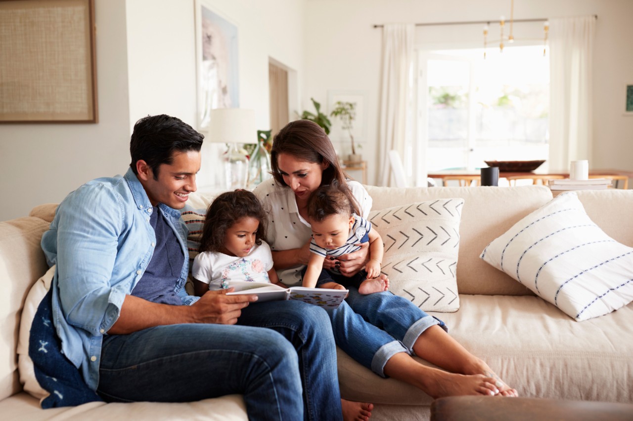 Hisanic couple reading a book on the sofa with their daughter